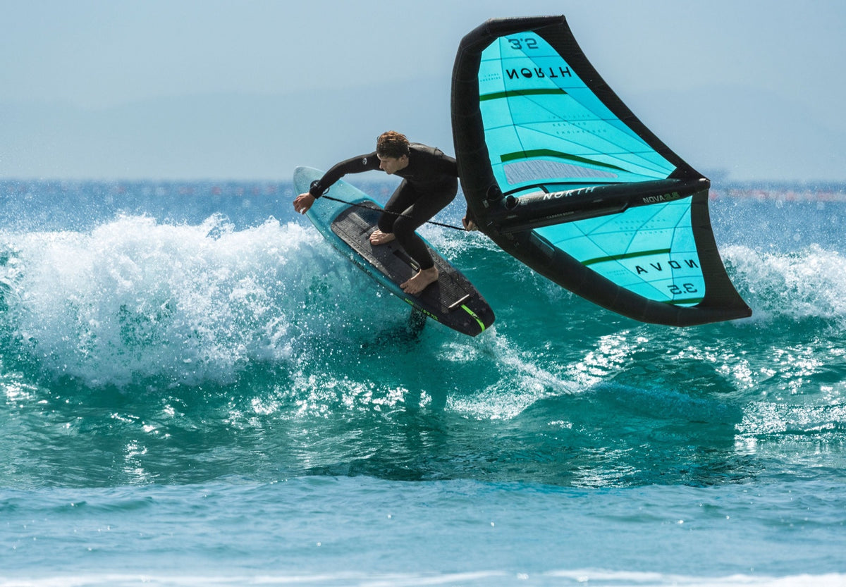 Wing foiler driving off the lip of a breaking wave