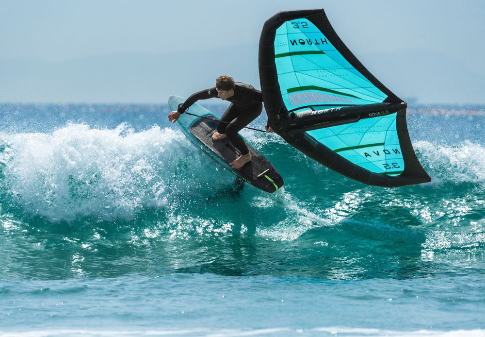 Wing foiler driving off the lip of a breaking wave