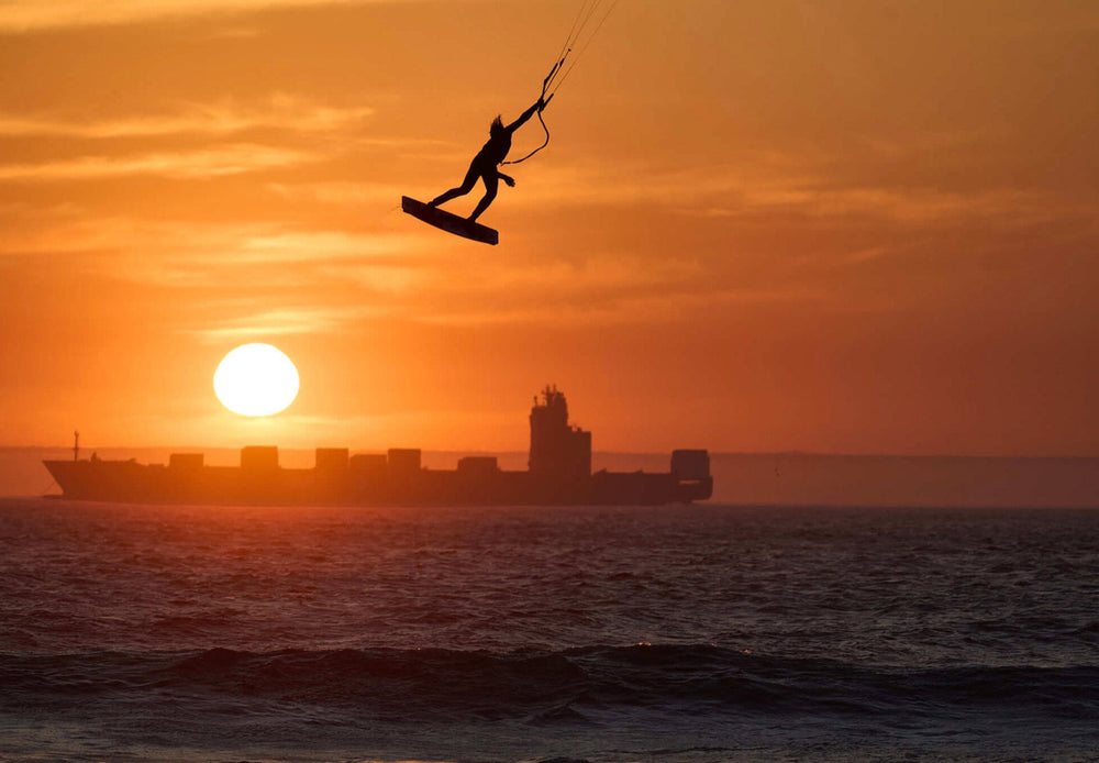 Kiteboarder silhouetted at the top of a big jump against a sunset